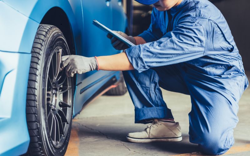 Inspector ITP ingenuncheaza pentru a verifica roata unei masini albastre, intr-un garaj, in cadrul unei inspectii ITP